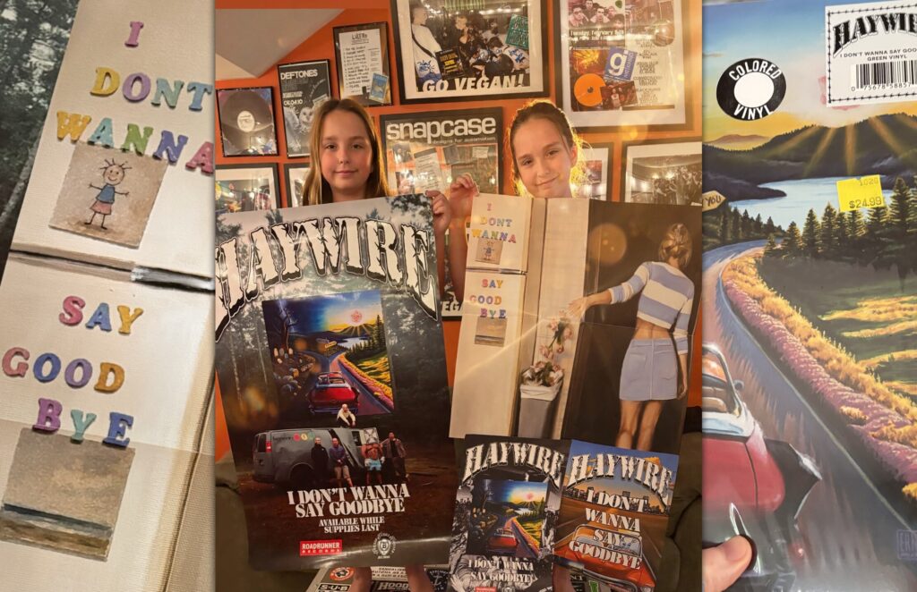 Two kids holding up Haywire I Don’t Wanna Say Goodbye posters in front of a wall of framed hardcore show memorabilia